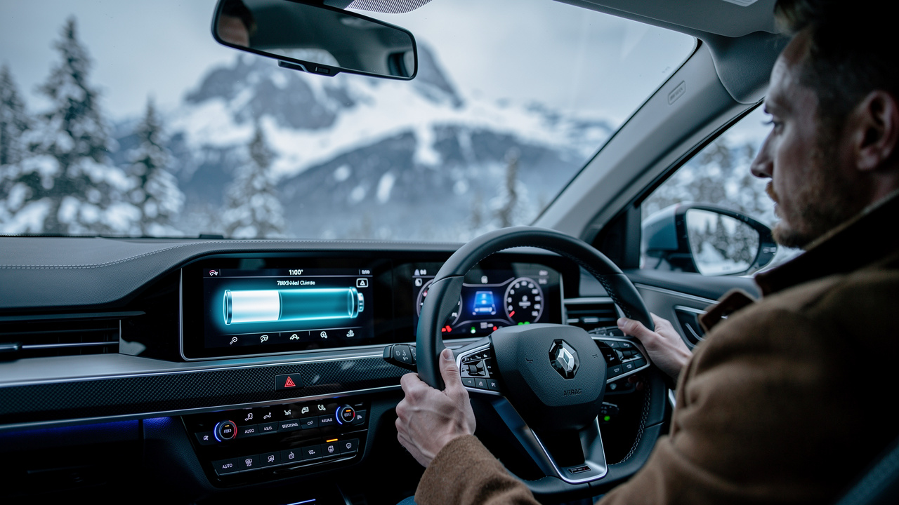 Tableau de bord lumineux d’une voiture électrique avec indicateurs d’autonomie et de préconditionnement, un conducteur en manteau observant un paysage hivernal enneigé.