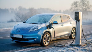 Voiture électrique compacte stationnée devant une borne de recharge, avec du givre sur le pare-brise, par une matinée d’hiver lumineuse.