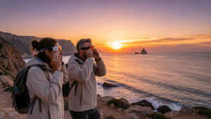 Deux femmes et un homme observent une éclipse solaire avec des lunettes de protection sur une côte espagnole au coucher du soleil.