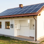 Maison individuelle bulgare équipée de panneaux photovoltaïques sur le toit et d’une batterie domestique murale dans un local technique lumineux.